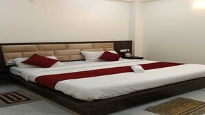 Una cama bien hecha con ropa de cama blanca y roja, un cabecero de madera y una mesita de noche con una lámpara.