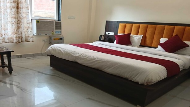 Una habitación de hotel con una cama grande, una mesita de noche, un equipo de aire acondicionado y una ventana con cortinas.