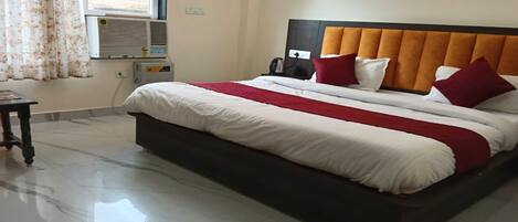 Una habitación de hotel con una cama grande, una mesita de noche, un equipo de aire acondicionado y una ventana con cortinas.