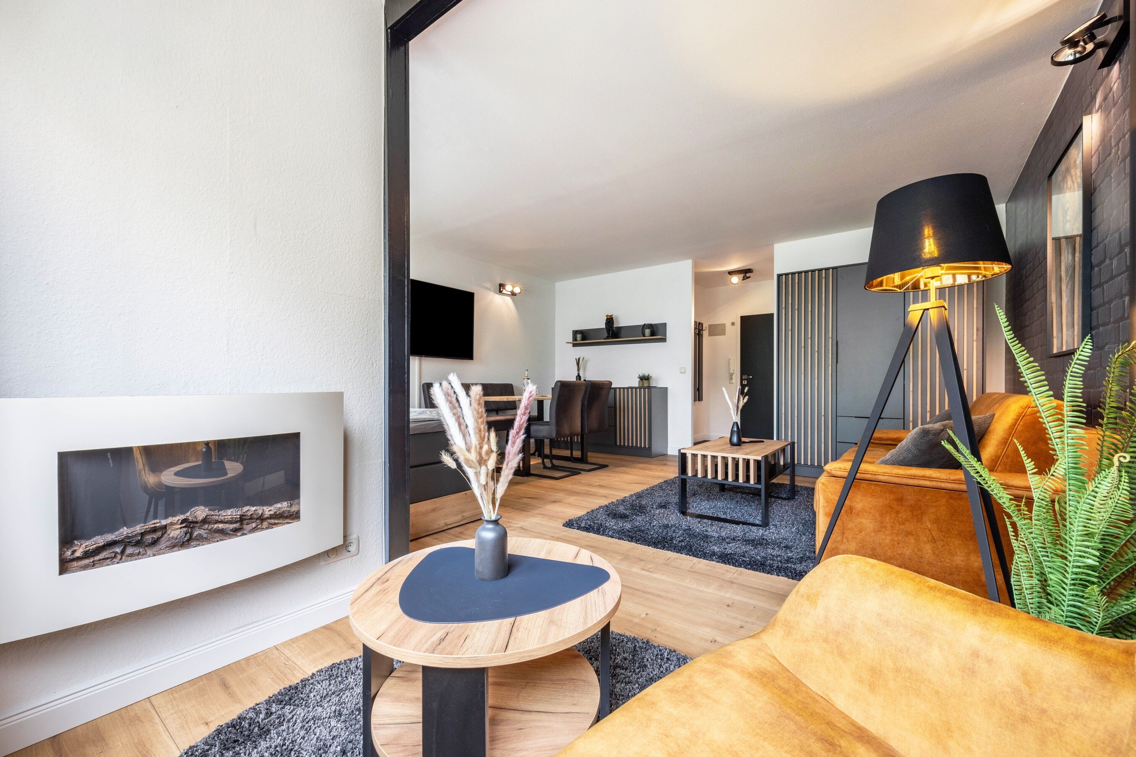 Ein modernes Wohnzimmer mit Kamin, einem runden Couchtisch, einer Couch, einer Stehlampe und einem Essbereich im Hintergrund.