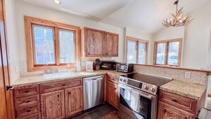 Una cocina moderna con armarios de madera, lavavajillas, microondas, horno y ventanas amplias.