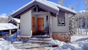 Un edificio cubierto de nieve con puerta de madera, base de piedra y cielo despejado.