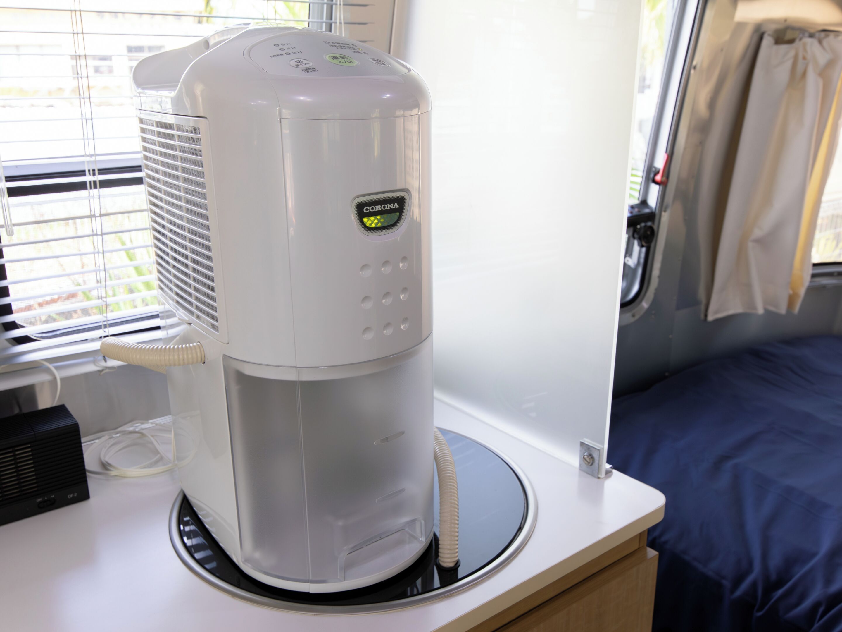 A white portable air conditioner with a control panel, placed on a table near a window with blinds.