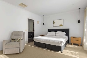 A bedroom with a bed, a chair, a nightstand, a dresser, and a door leading to a bathroom.