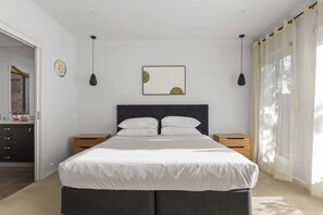 A bedroom with a large bed, two bedside tables, a wall clock, and a window with curtains.