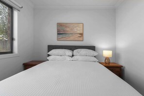 A bedroom with a bed, a nightstand, a lamp, and a painting on the wall.