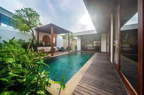 Un área de piscina exterior moderna con cubierta de madera, sillones de descanso y un pérgola.