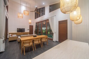 Un salón amplio con una mesa de comedor, sillas de mimbre, un sofá, un televisor y un balcón con puerta de vidrio.