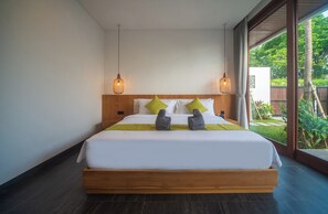 Ein großes Bett mit Holzrahmen, weißer Bettwäsche und zwei grünen Kissen. An beiden Seiten des Bettes befinden sich zwei hängende Leuchten.