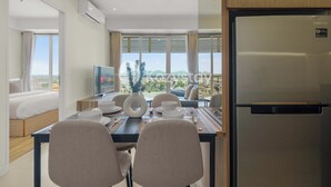 A modern hotel room with a dining area, a bed, a TV, and a Samsung refrigerator. - Tirava by Kozystay - Paskal (Bandung)