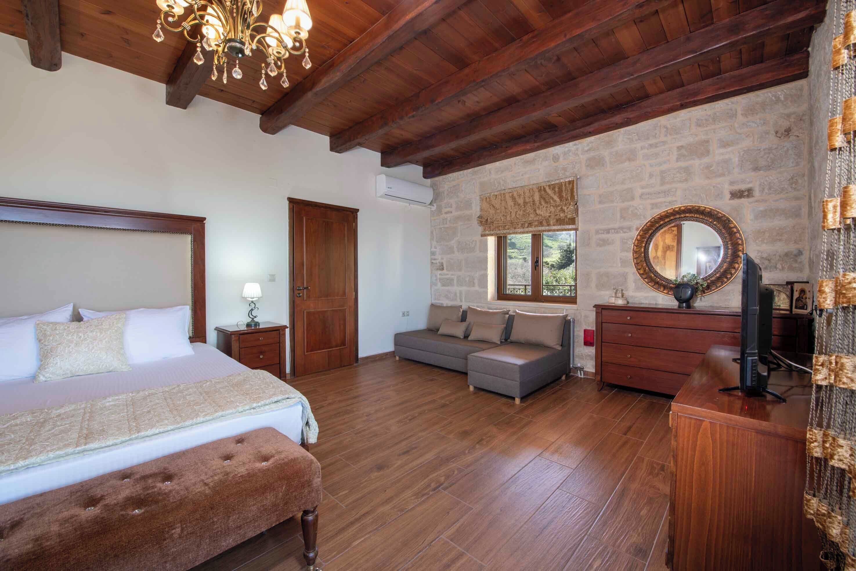 A bedroom with a large bed, a sofa, a wooden dresser, and a stone wall.