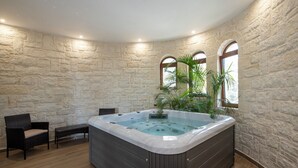 A spa room with a stone wall, a hot tub, two chairs, and a bench.