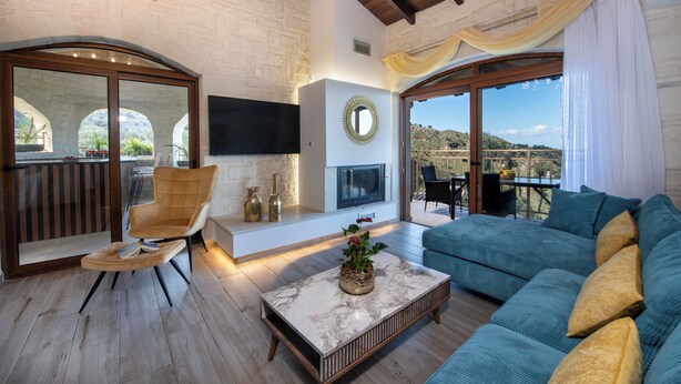 A spacious living area with a large sofa, a comfortable armchair, a marble coffee table, and a flat-screen TV mounted on the wall.