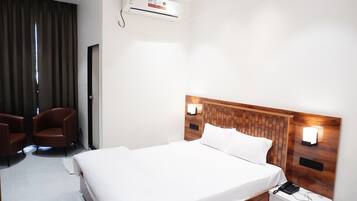 Habitación de hotel con una cama grande, dos mesitas de noche, aire acondicionado de pared y un par de sillas.