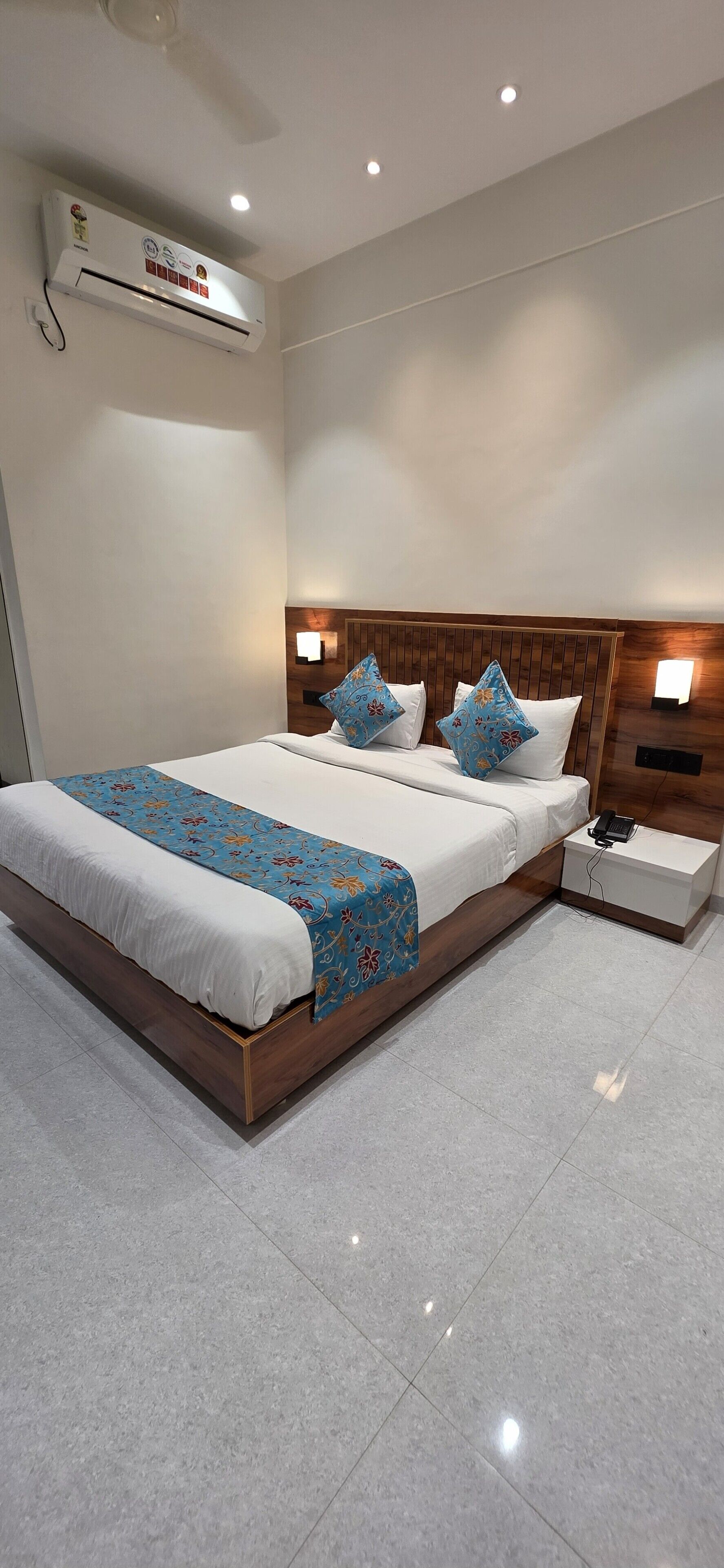 A hotel room with a bed, bedside lamps, a phone on the nightstand, and an air conditioning unit.