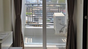Una habitación con un amplio ventanal corredera que da a un balcón. Hay un escritorio blanco y una alfombra estampada en el suelo.