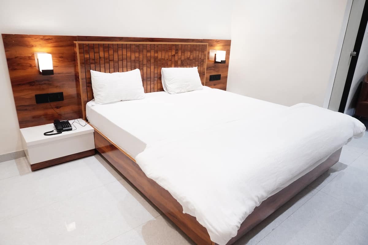 A modern hotel room with a wooden headboard, two bedside tables, a white bed, and wall-mounted lights.