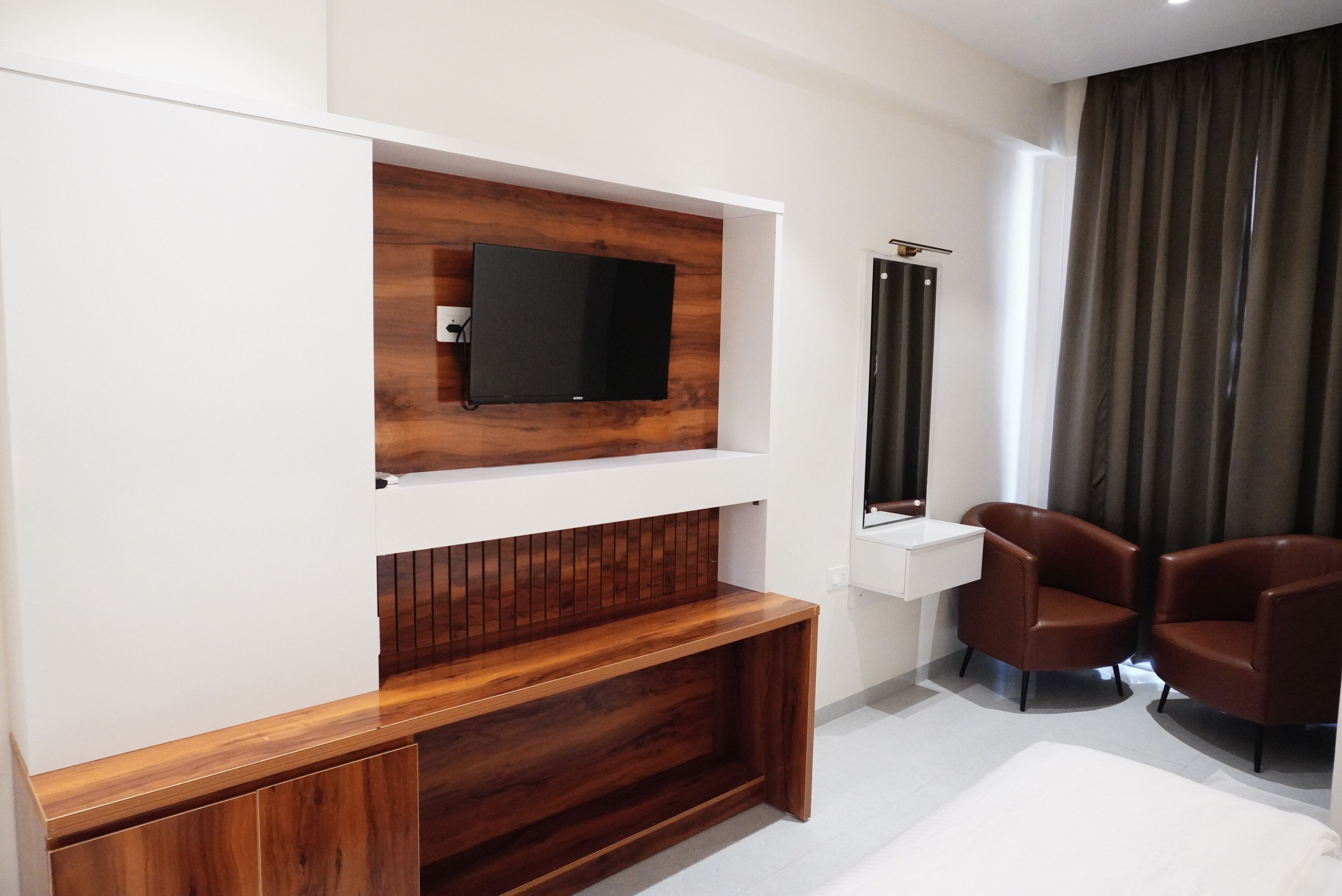 Ein modernes Hotelzimmer mit einer Wandpaneele aus Holz, einem Flachbildfernseher, einem Schminktisch mit Spiegel und zwei Ledersesseln.