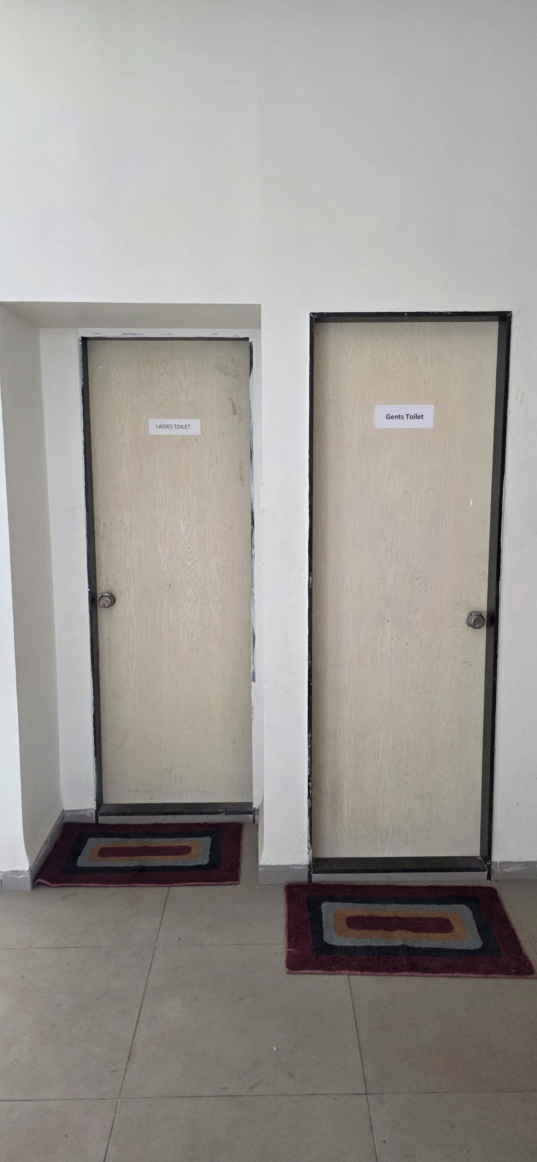Two doors labeled "Ladies Toilet" and "Gents Toilet" with a tiled floor and a doormat in front of each door.