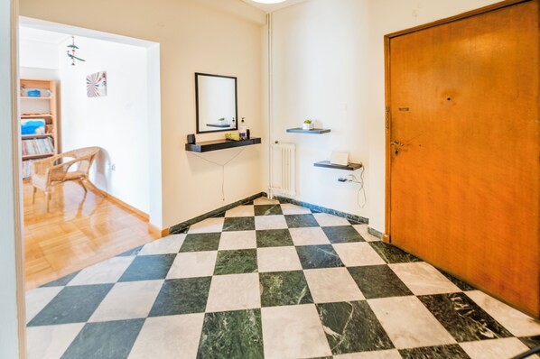 A hotel room with a checkered floor, a wooden door, a radiator, and a shelf with toiletries.