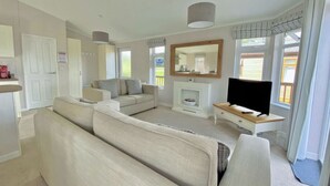 A modern living room with a sofa, TV, fireplace, and large windows. - 1 bedroom accommodation in Tunstall, Richmond (Tunstall, Richmond)