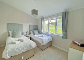 Un dormitorio con dos camas, una mesita de noche con lámpara, una ventana con cortinas y una lámpara en el techo.