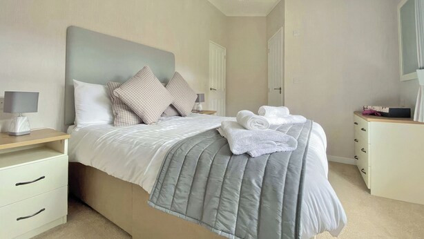 A neatly made bed with pillows, a bedside lamp, a dresser, and a mirror. - 1 bedroom accommodation in Tunstall, Richmond (Tunstall, Richmond)