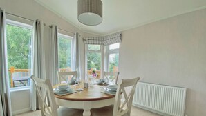 A dining room with a round table set for four, white chairs, a ceiling light fixture, and a view of greenery outside. - 1 bedroom accommodation in Tunstall, Richmond (Tunstall, Richmond)