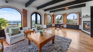 A spacious living room with a fireplace, large windows, and a view of the ocean.