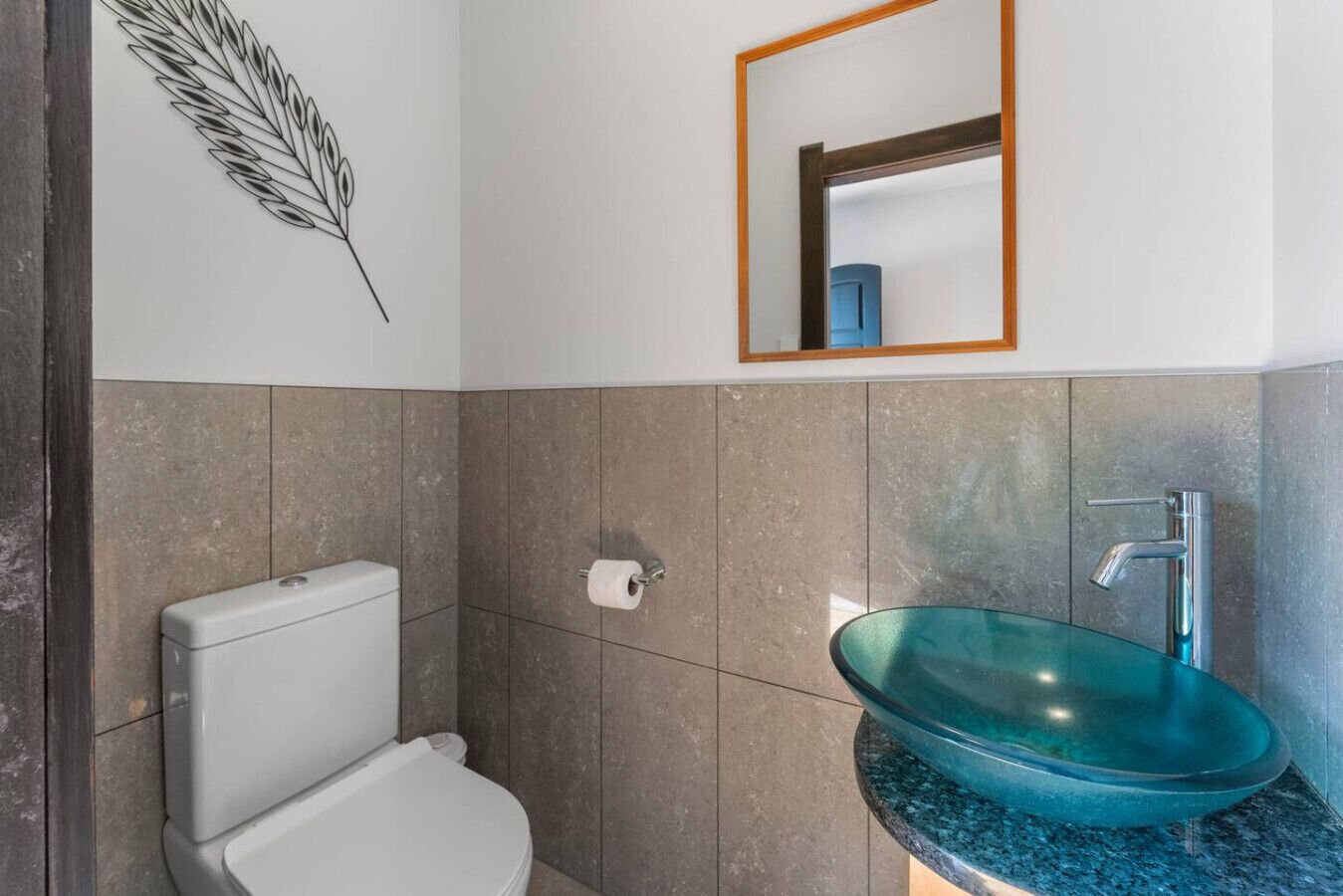Une salle de bain moderne avec des toilettes blanches, un lavabo en verre et un miroir au-dessus du lavabo.