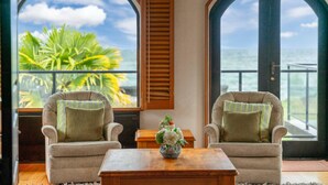 A room with two armchairs, a wooden coffee table, and a view of the ocean through large arched windows.