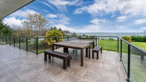 A covered patio with a table and benches, overlooking a grassy area and the sea.