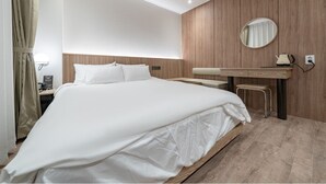 Een moderne hotelkamer met een groot bed, houten paneelwanden, een ronde spiegel, een klein tafeltje en een nachtkastje.