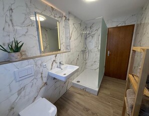 A bathroom with a marble wall, a white sink, a mirror, and a shower area. - Moderne Ferienwohnung in Elstra (Elstra)
