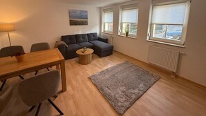 Uma sala de estar moderna com uma mesa de jantar de madeira, sofá cinza e uma pequena mesa de centro redonda.