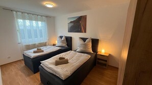 Quarto com duas camas, janela com cortinas leves, um quadro na parede e abajures.