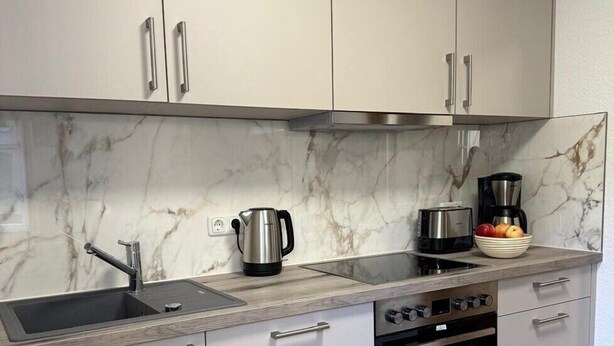 Uma cozinha moderna com armários brancos, painel de fundo de mármore, pia de aço inoxidável, cafeteira e forno.