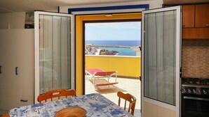 A balcony with a table and chairs, a view of the sea, and a kitchen area. - Vista mare, ampio terrazzo e aria condizionata (Castelsardo SS)
