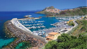 A coastal marina with boats, a fortified hilltop, and a curved road leading to a building. - Vista mare, ampio terrazzo e aria condizionata (Castelsardo SS)