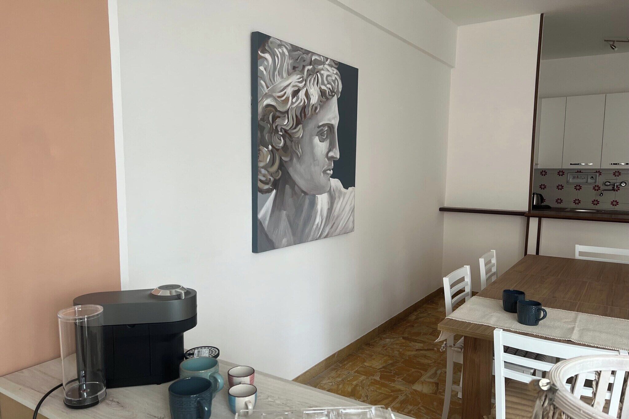 Un comedor con una mesa preparada para dos, una cafetera y una obra de arte colgada en la pared.