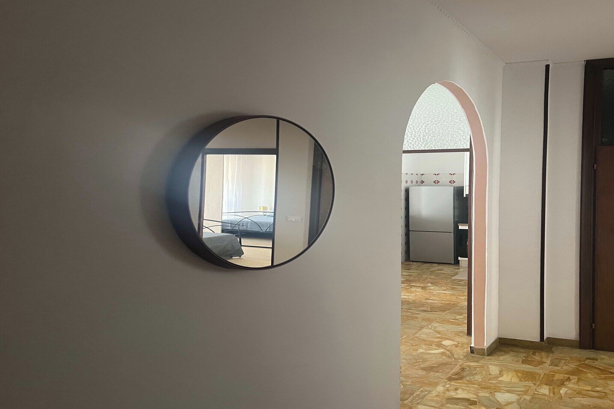 Un pasillo con un espejo redondo en la pared, que conduce a una habitación con cama y ventana.