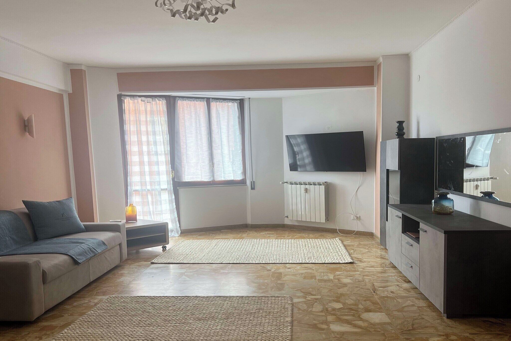 A living room with a sofa, a TV, a radiator, and a window with curtains.
