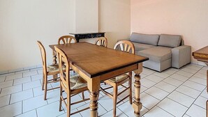 A dining area with a wooden table and chairs, a grey sofa, and a tiled floor.