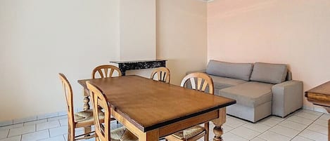 A dining area with a wooden table and chairs, a grey sofa, and a tiled floor.