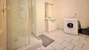 A bathroom with a glass shower enclosure, a sink, and a washing machine.