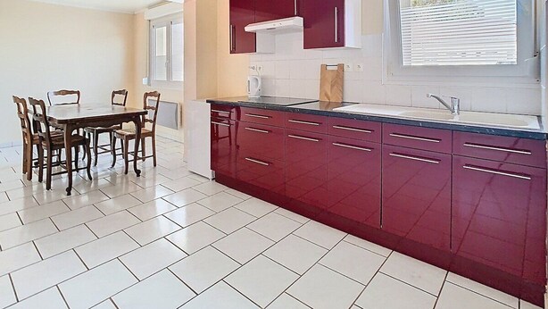 A kitchen with a dining table and chairs, red cabinets, and a window with blinds.