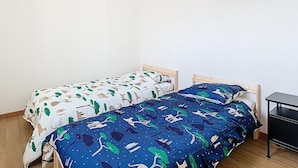 A dormitory room with two single beds, wooden headboards, and a small black nightstand.