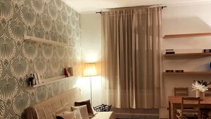 Ett sovrum med en säng, ett sängbord, en lampa, ett element och ett fönster med gardiner.