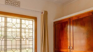 Quarto com cama, janela com padrão geométrico, guarda-roupa de madeira e ventilação no teto.