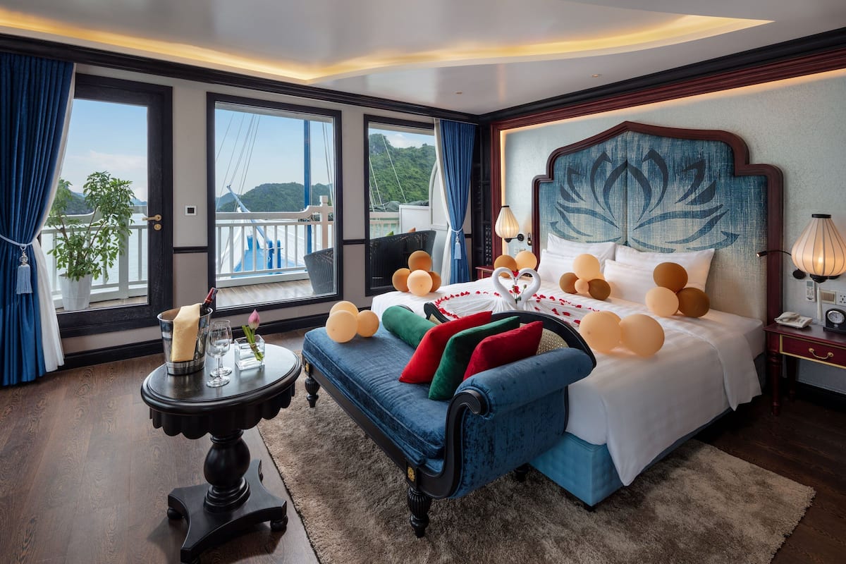 A bedroom with a large bed, a side table, a view of the outdoors, and a balcony.